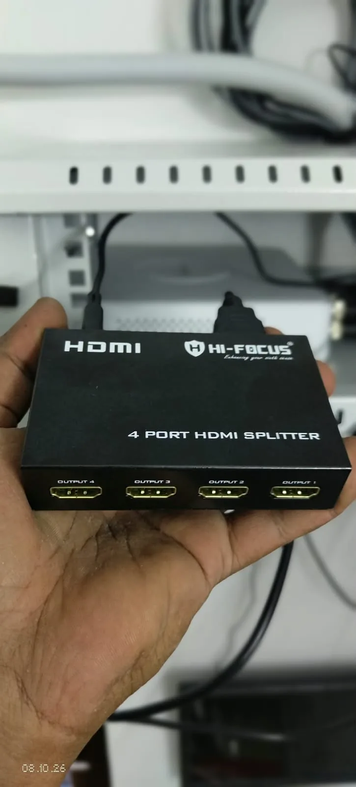 HI-FOCUS four-port HDMI splitter held in front of equipment shelving